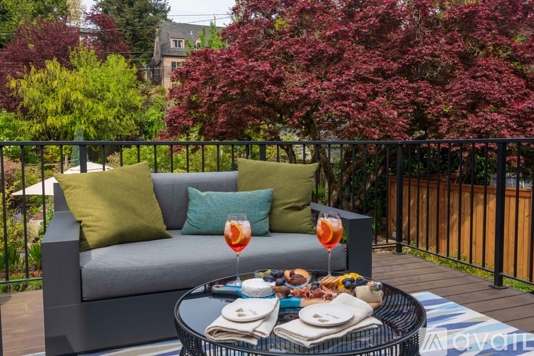 A grey couch with green pillows and a glass of orange juice on a table.