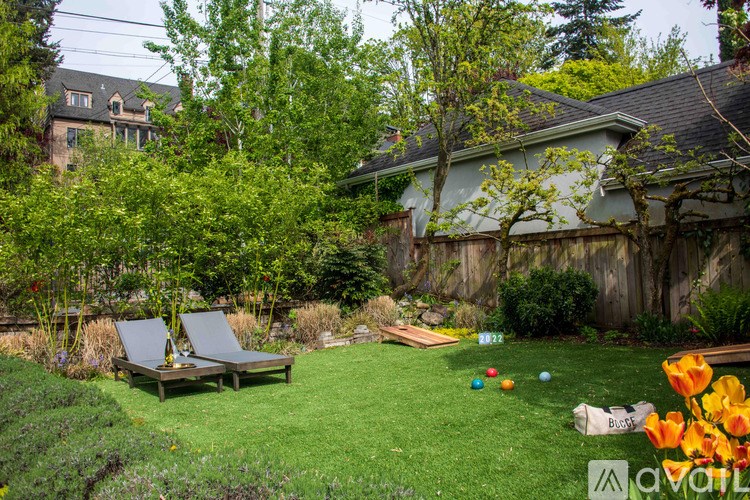 A backyard with a lawn, two lounge chairs, and a fence.