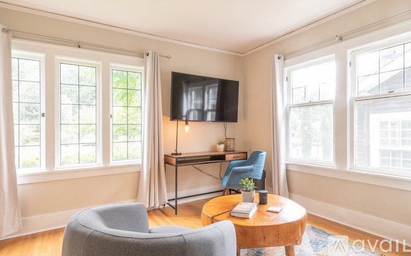 A living room with a grey armchair, a wooden coffee table, and a television on the wall.