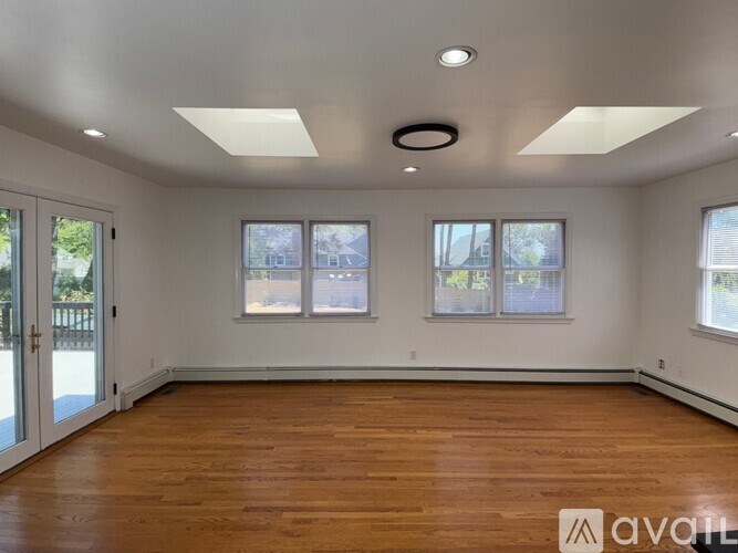 A spacious room with wooden floors and three windows.