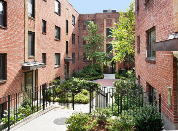 a courtyard between two red brick buildings with trees and bushes
