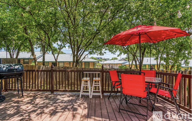 A red umbrella is on a wooden deck with chairs and a grill.