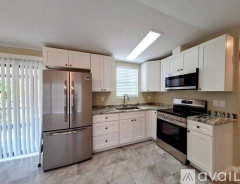 A kitchen with a stainless steel refrigerator, white cabinets, and a granite countertop.