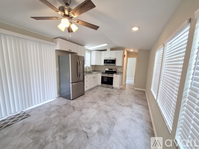 A kitchen with a refrigerator, oven, and a fan on the ceiling.