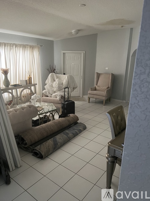 A room with a white sofa, a chair, and a table with a vase on it.