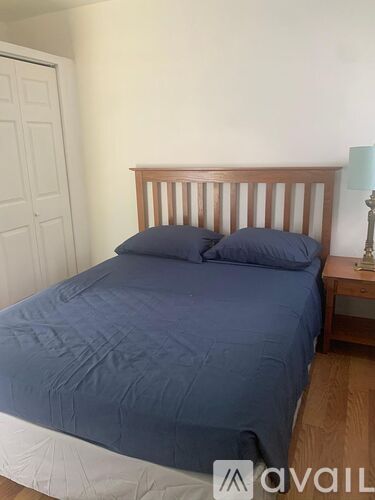 A bed with a blue comforter and two pillows sits in a room with a wooden headboard.
