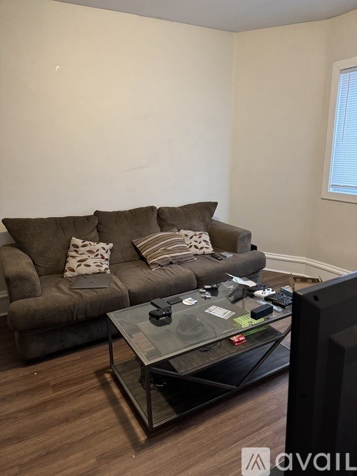A living room with a brown couch, a glass coffee table, and a TV.