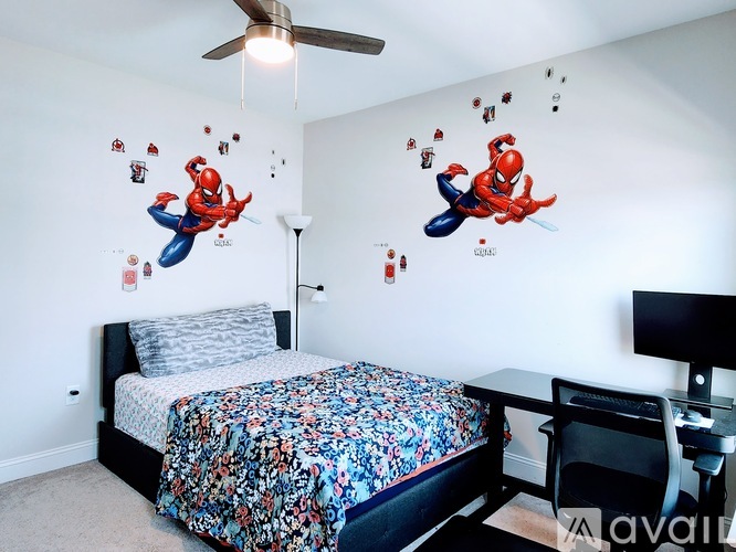 A bedroom with a Spider-Man wall decal and a bed with a floral comforter.