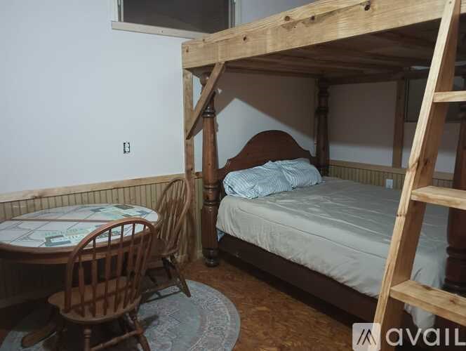 A wooden bunk bed with a ladder is in a room with a table and chair.