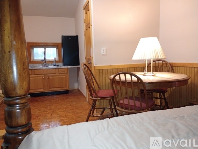 A bedroom with a bed, a table with chairs, and a kitchen area with a refrigerator and sink.