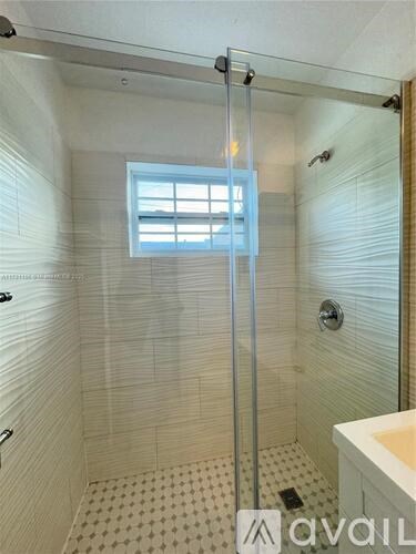 A bathroom with a glass shower door and a window.
