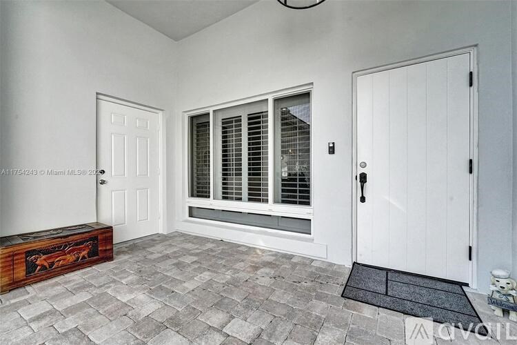 A room with a white door, a window with blinds, and a bench with a painting on it.