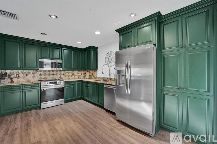 A kitchen with green cabinets and a stainless steel refrigerator.