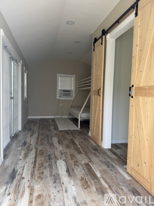 A room with wooden flooring and a white ceiling with a window on the left.