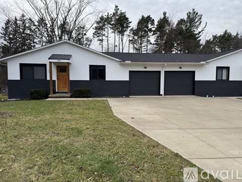 A white house with a black garage door is in front of a wooded area.