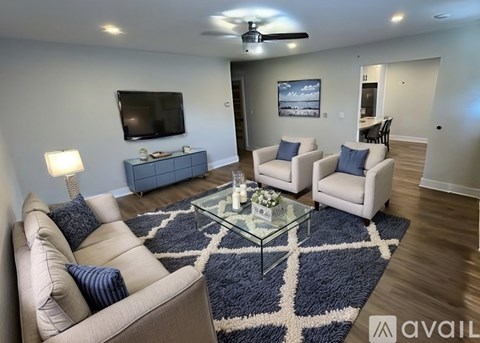 A living room with a beige couch, a glass coffee table, and a television on the wall.