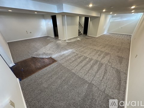 A spacious room with a carpeted floor and a staircase in the background.