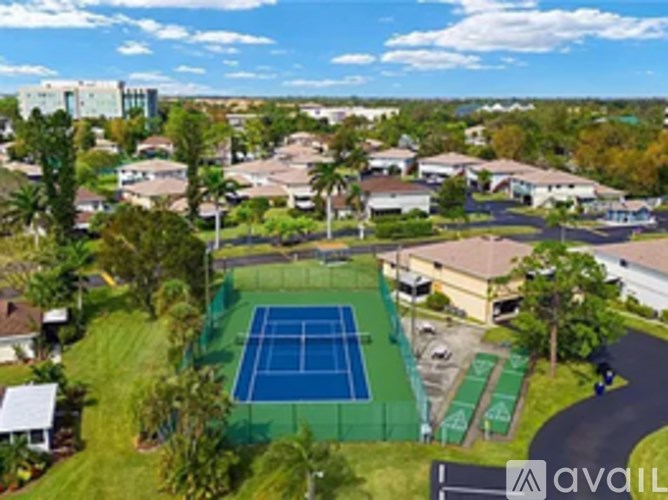 A tennis court is surrounded by houses and trees.