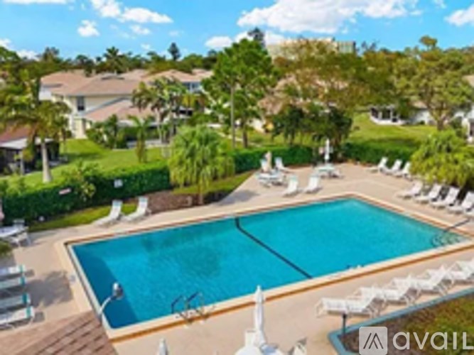 A pool surrounded by lawn chairs and trees.
