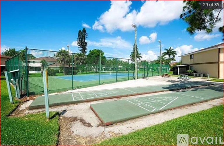 A tennis court is surrounded by a green fence and has a clear blue sky above it.