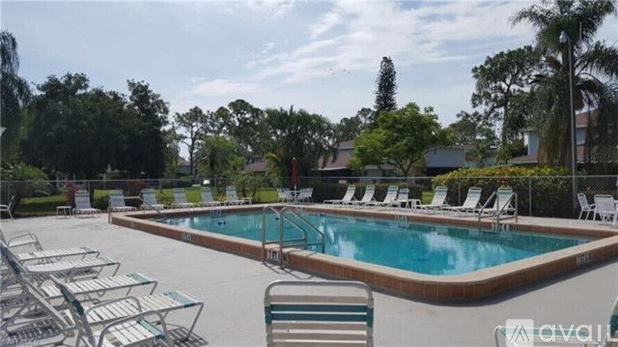 A pool surrounded by chairs and trees.