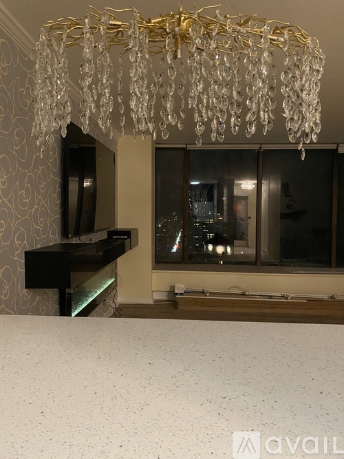 A chandelier with a gold frame and clear crystals hangs over a piano in a room with a patterned wallpaper.