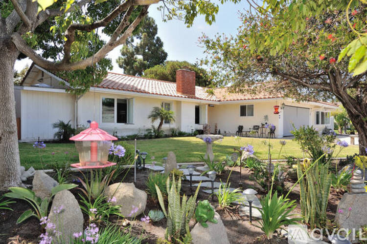 A white house with a red roof and a garden in front.