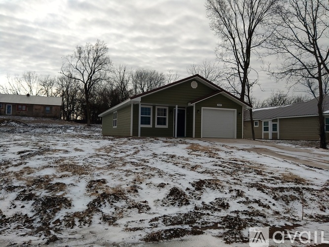 A house in a snowy field with trees in the background.