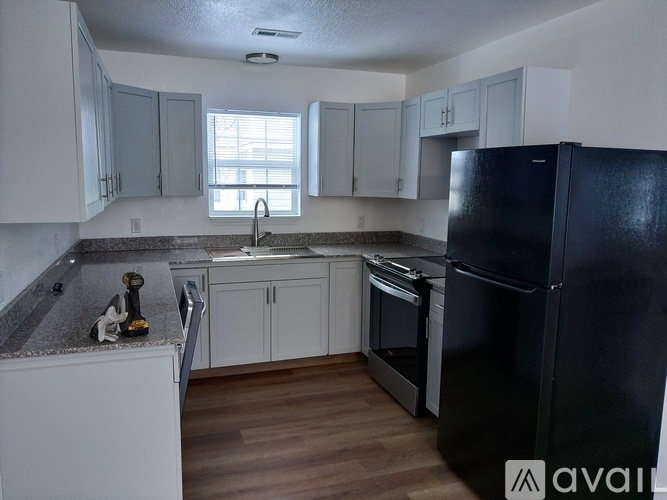 A kitchen with a black refrigerator, white cabinets, and a granite countertop.