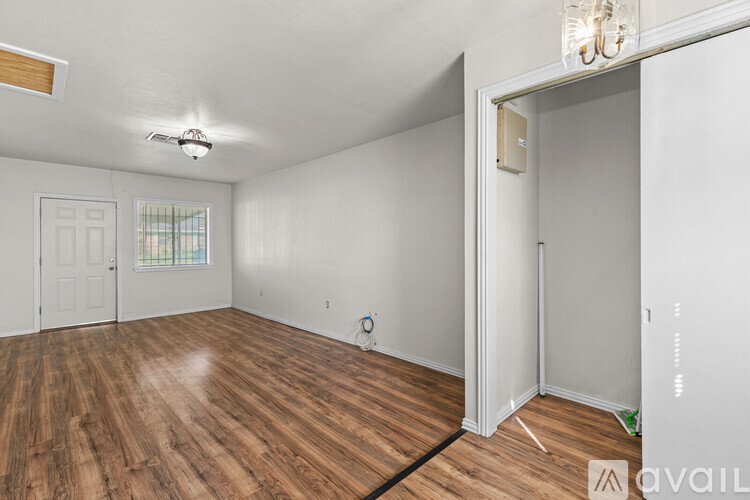 A room with wooden flooring and white walls, with a door on the right side.