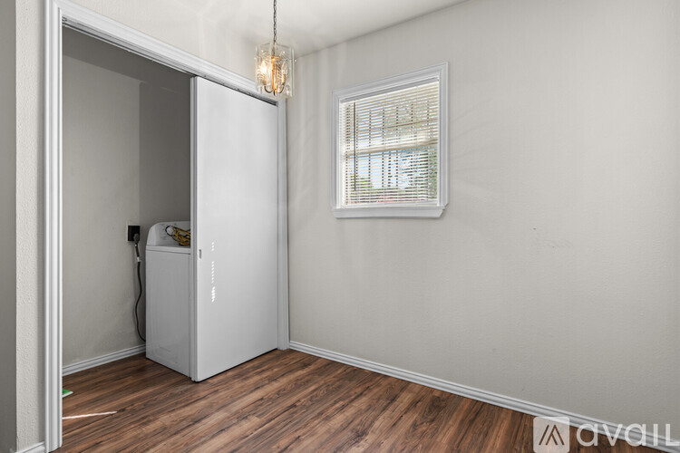 A small room with a white door, a window with blinds, and a wooden floor.