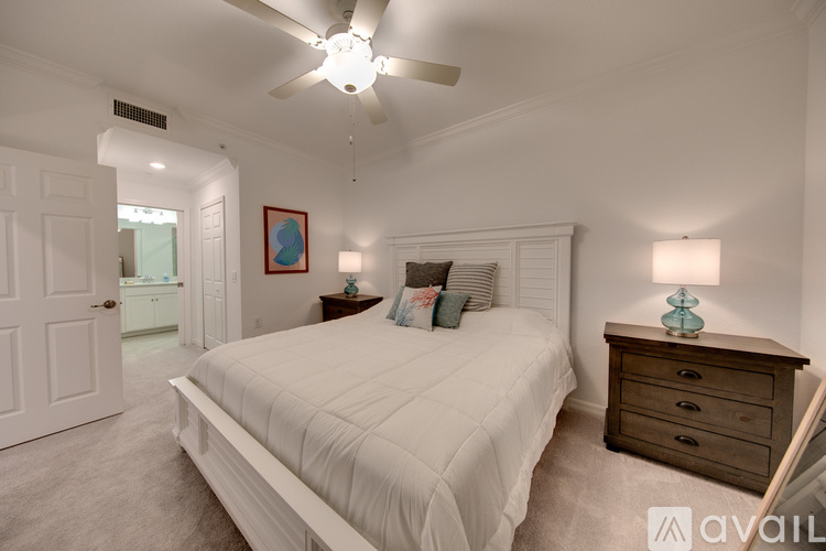 A bedroom with a large bed, a ceiling fan, and a dresser with a lamp on top.