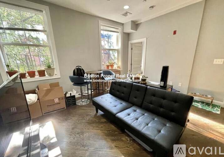 A living room with a black couch and boxes on the floor.