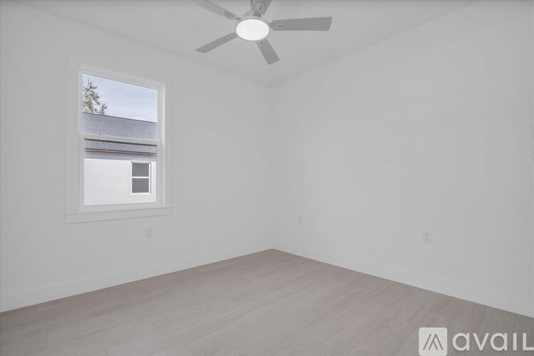A room with a ceiling fan and a window overlooking a building.