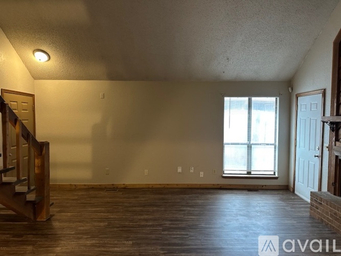 A spacious room with wood flooring and a window with blinds.