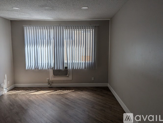 A room with a window covered by white blinds and wooden flooring.