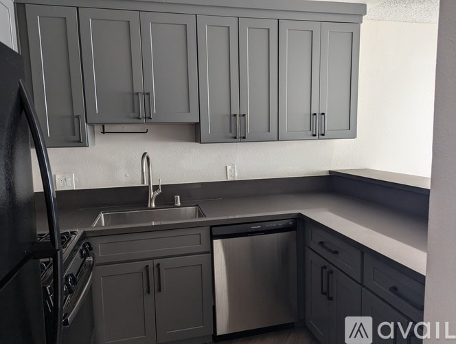 A kitchen with grey cabinets and a black refrigerator.