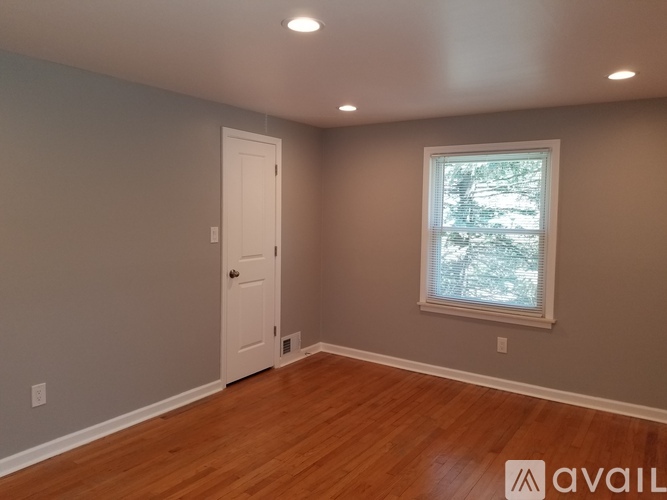 A room with a white door and a window with a view of trees outside.