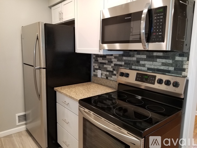 A kitchen with a black fridge, white cabinets, a stove, and a microwave.