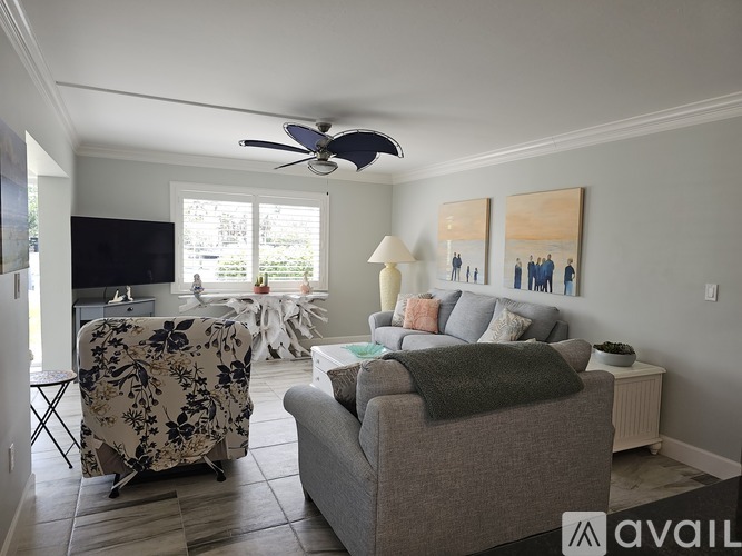 A living room with a grey couch, a fan, and a painting on the wall.