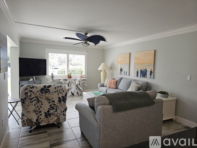 A living room with a grey couch, a fan, and a painting on the wall.