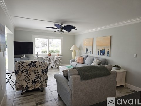A living room with a grey couch, a fan, and a painting on the wall.