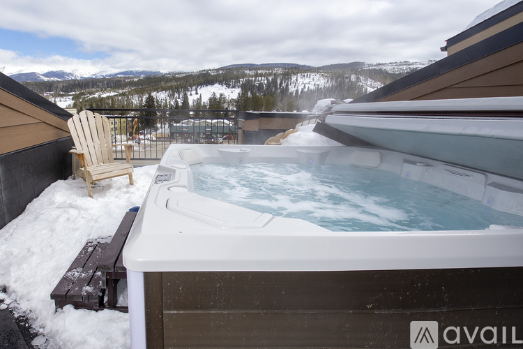A hot tub on a balcony with snow on the ground and mountains in the background.