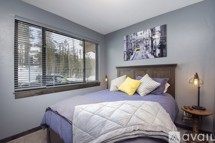 A bedroom with a bed, a window with blinds, a lamp, and a picture on the wall.