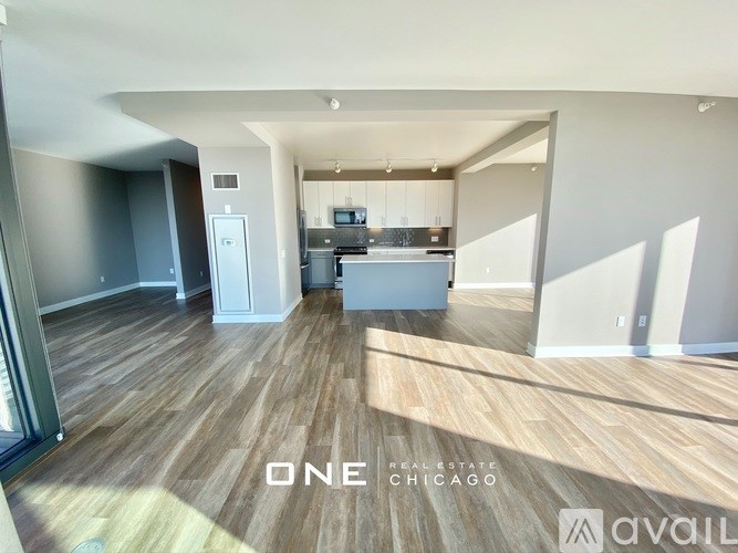 A spacious living room with wood flooring and a kitchen area in the background.