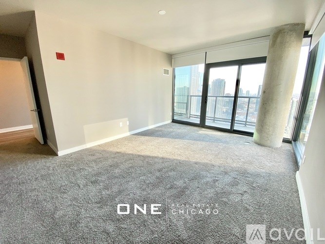 A room with a carpeted floor and a view of the city through large windows.