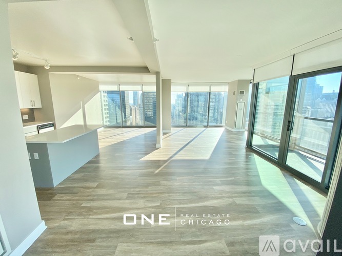 A spacious, well-lit room with wooden flooring and large windows overlooking a cityscape.