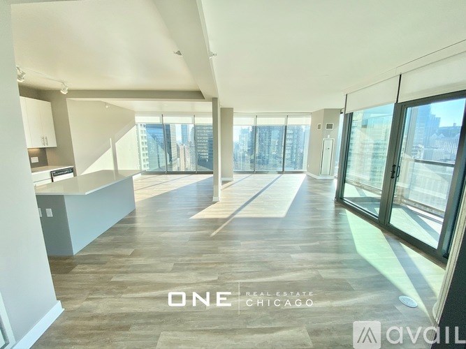 A spacious, well-lit room with wooden flooring and large windows overlooking a cityscape.