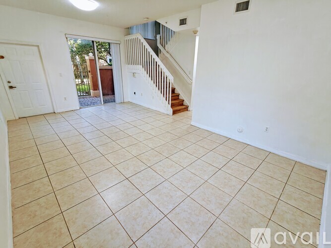 A spacious living room with tiled flooring and a staircase leading to the upper level.