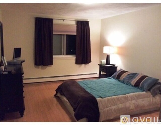 A bedroom with a bed, a desk, and a window with curtains.